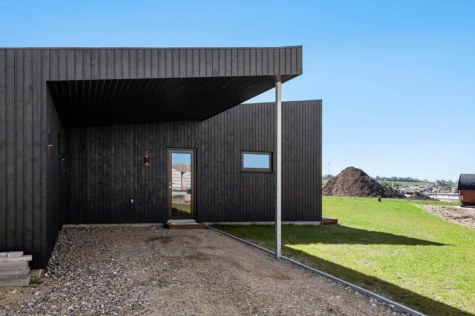 Modern wooden cabin with entrance door and window. Lawn and construction sites in background.