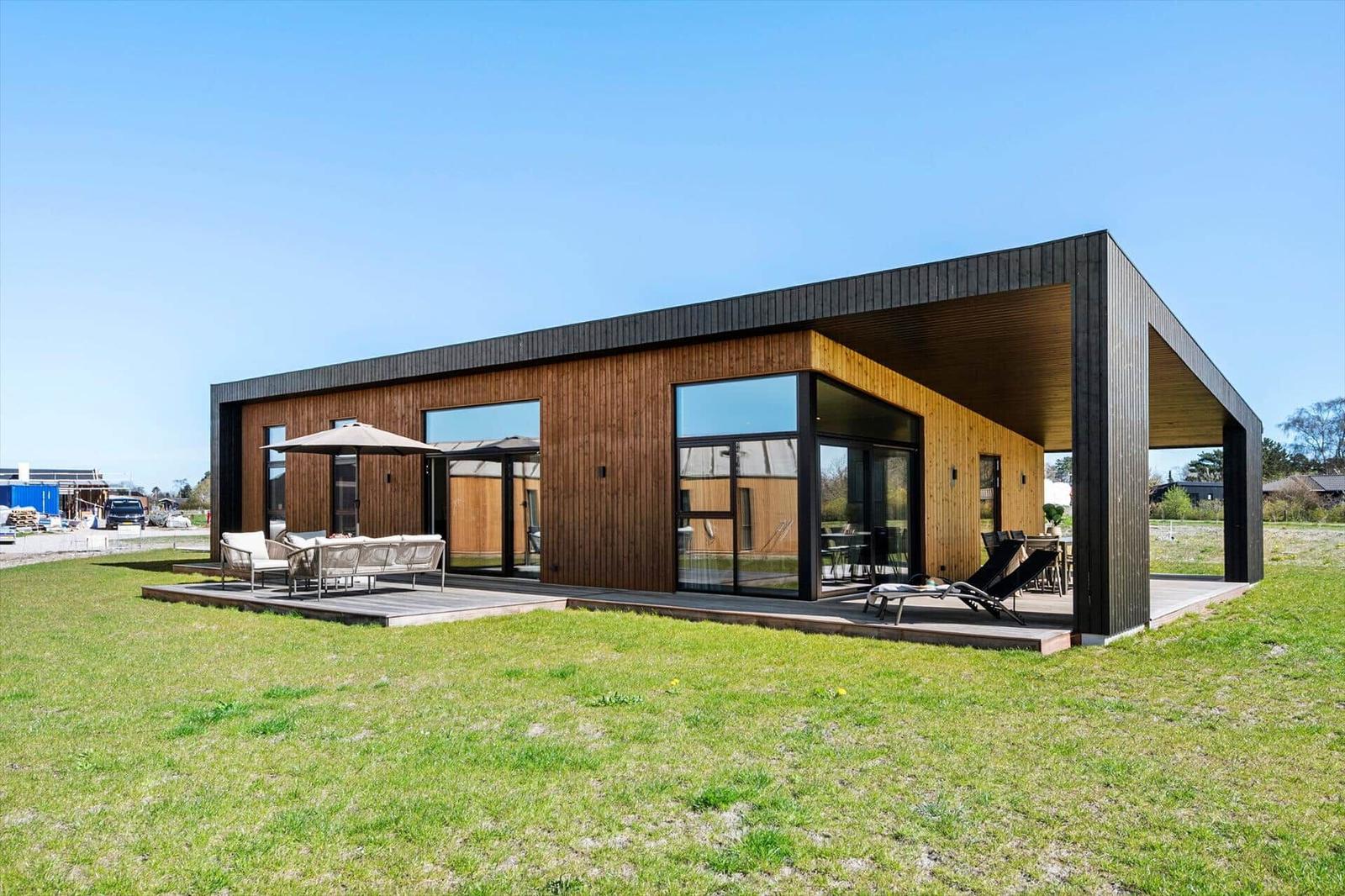 Modern wooden house with large deck and garden. Outdoor seating and lounge chairs.