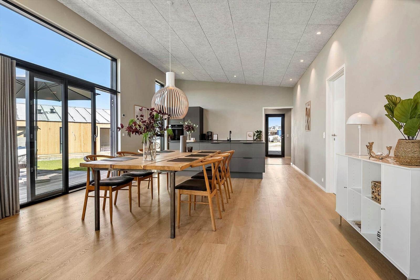 Dining area with wooden table and chairs. Kitchen and terrace are visible.