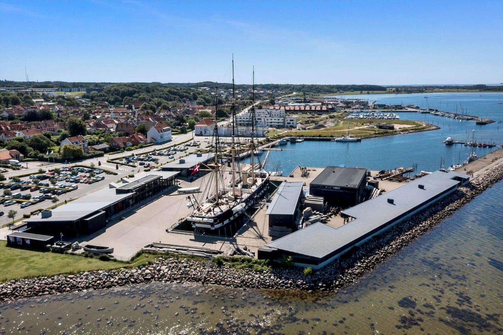 Harbor with sailboat, modern buildings, and boats in the background.