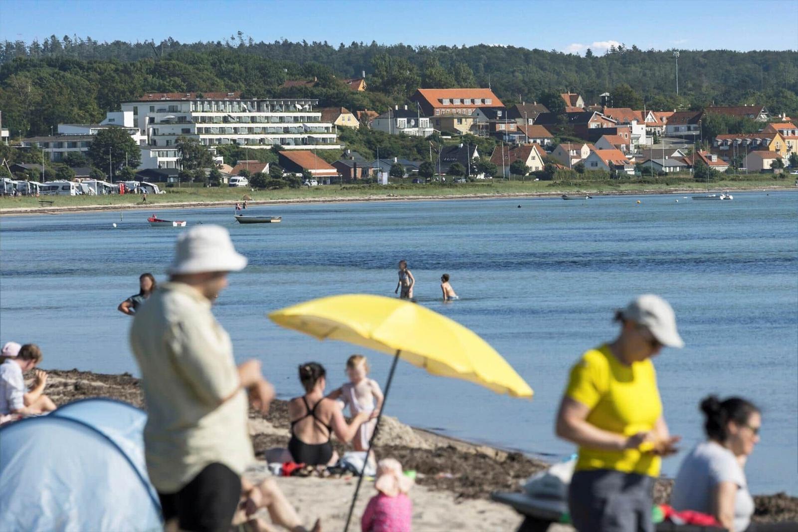 Beach with bathers, yellow umbrella, and view of houses by the water.