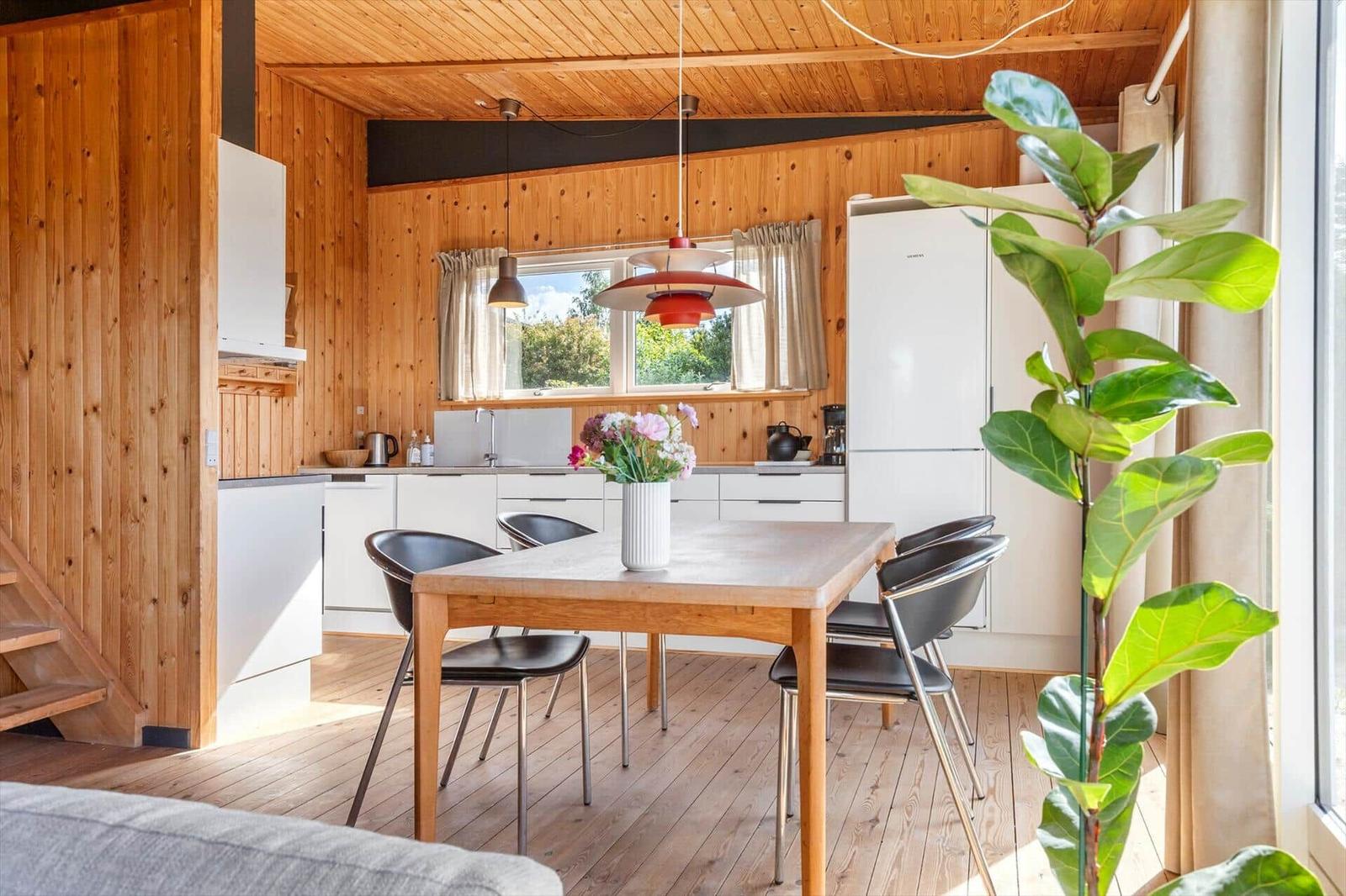 Dining area with wooden table, black chairs, and window view. Kitchen with white cabinets and refrigerator.