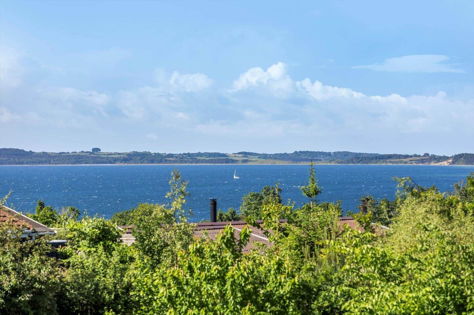 View of the sea with a sailboat and green vegetation in the foreground.