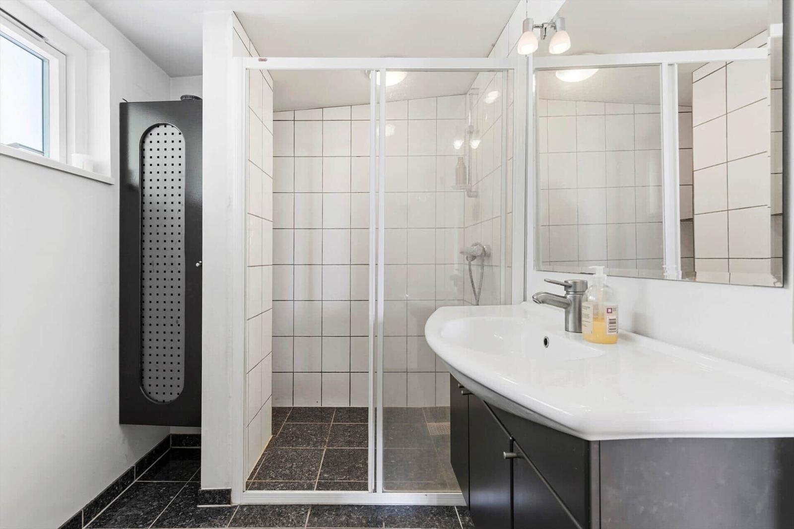 Bad mit Dusche, Waschbecken und Spiegel. Schwarze Fliesen und weiße Wände.