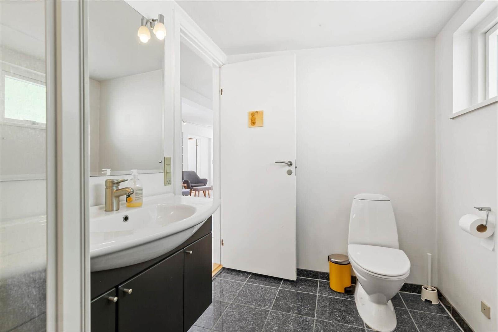 Badezimmer mit Waschbecken, Spiegel, Toilette und Fenster.