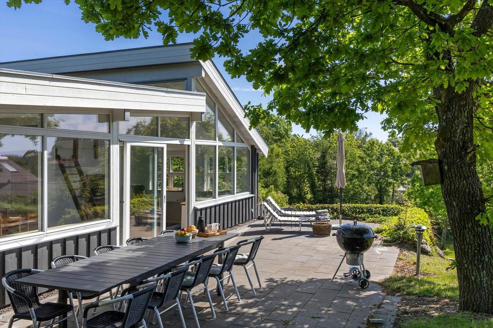 Terrasse mit Tisch, Stühlen, Grill und Liegen unter Bäumen.