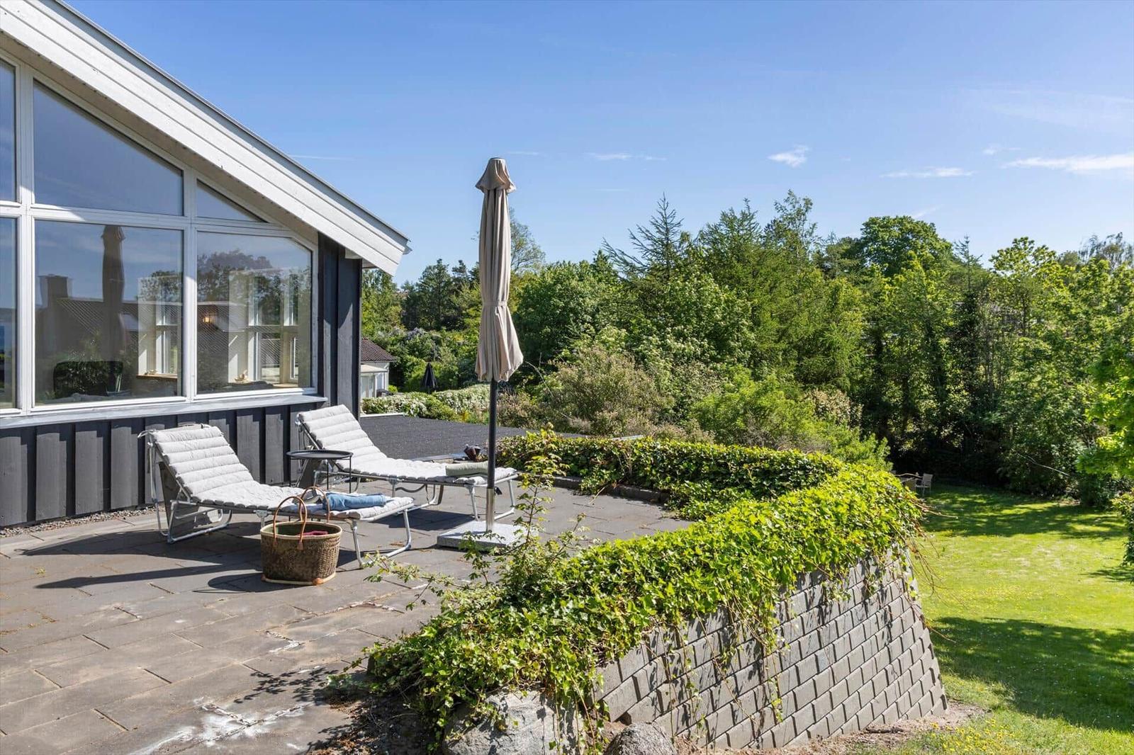 Terrasse mit Liegen, Sonnenschirm und Blick auf grüne Landschaft.