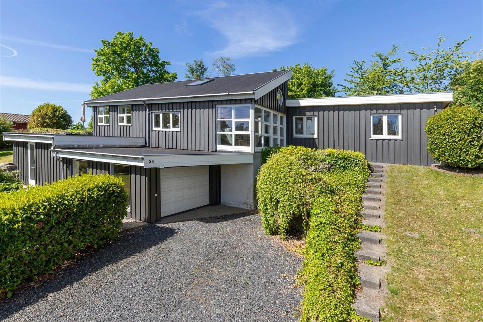 Moderne Villa mit Garage und grüner Umgebung unter blauem Himmel.