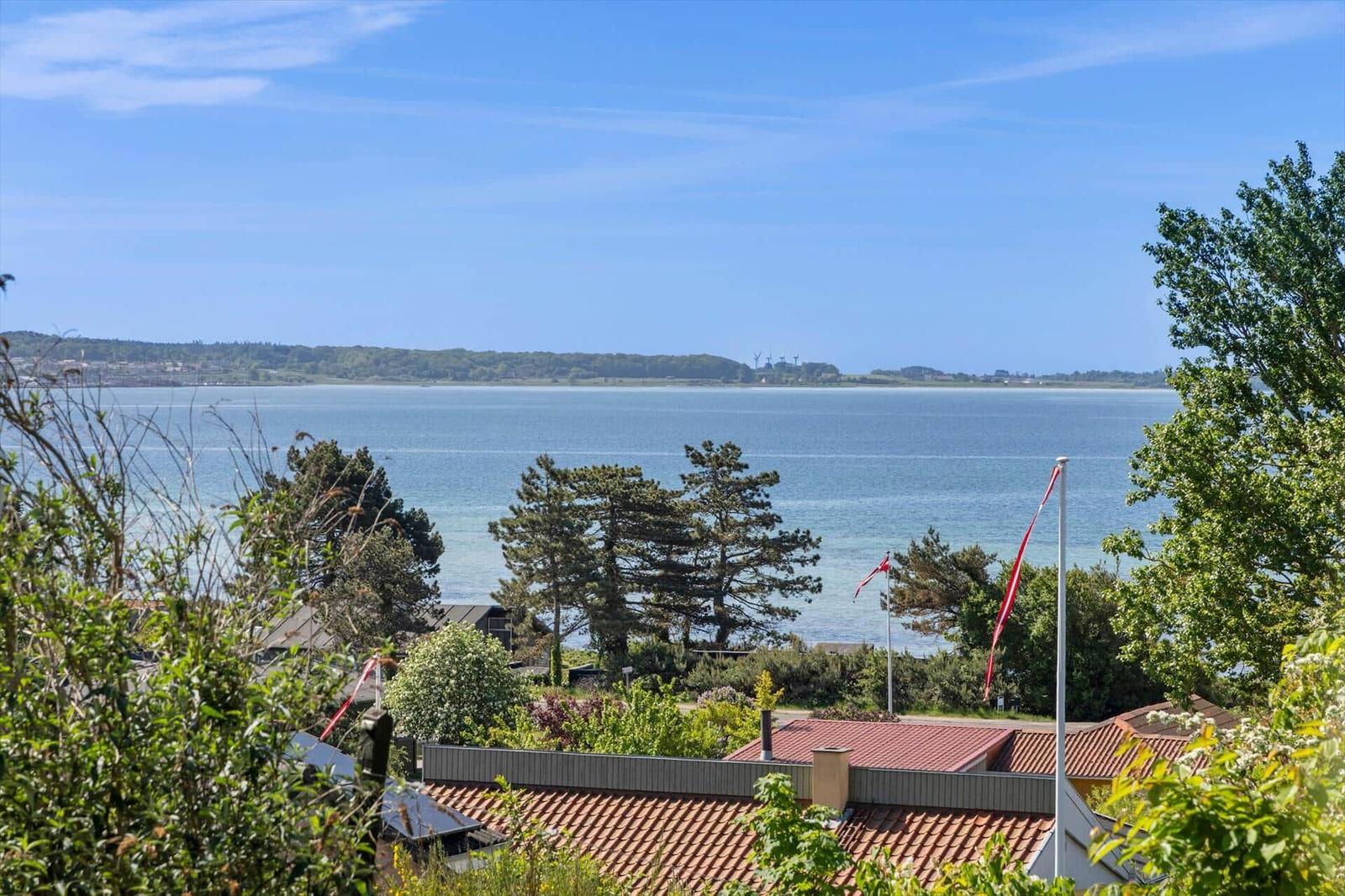 Weitläufiger Blick auf See und Küstenlinie mit Bäumen und Flaggen im Vordergrund.