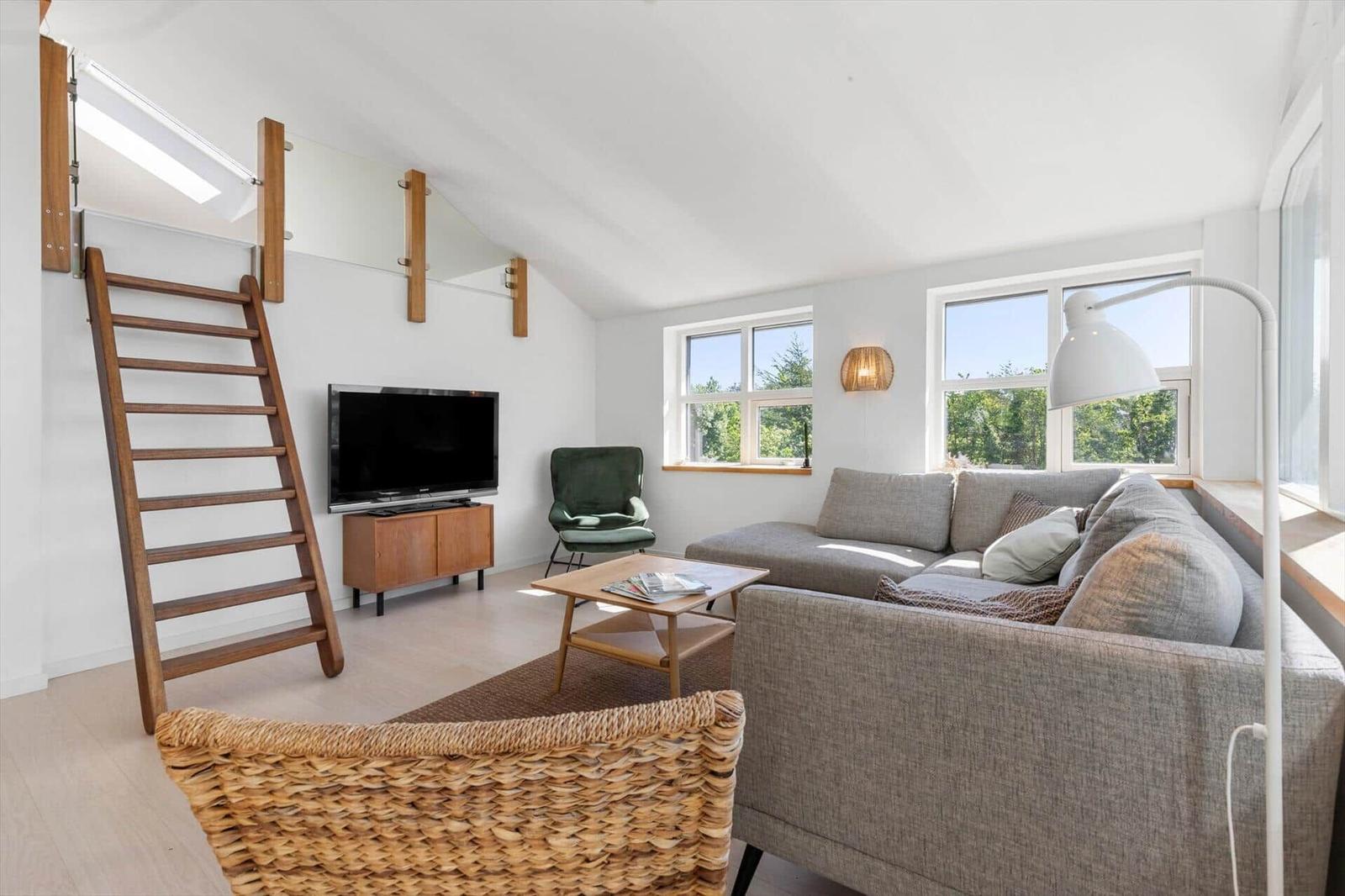 Wohnzimmer mit Sofa, Fernseher und Holztreppe zu einer oberen Ebene.