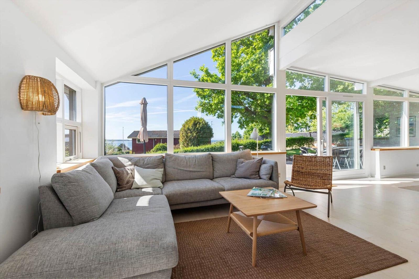 Wohnzimmer mit großem Sofa, Holztisch und Blick auf Grünflächen.