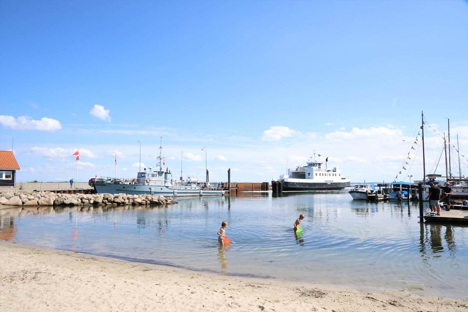 Two children are swimming in the harbor. Ships and a dock are visible in the background.