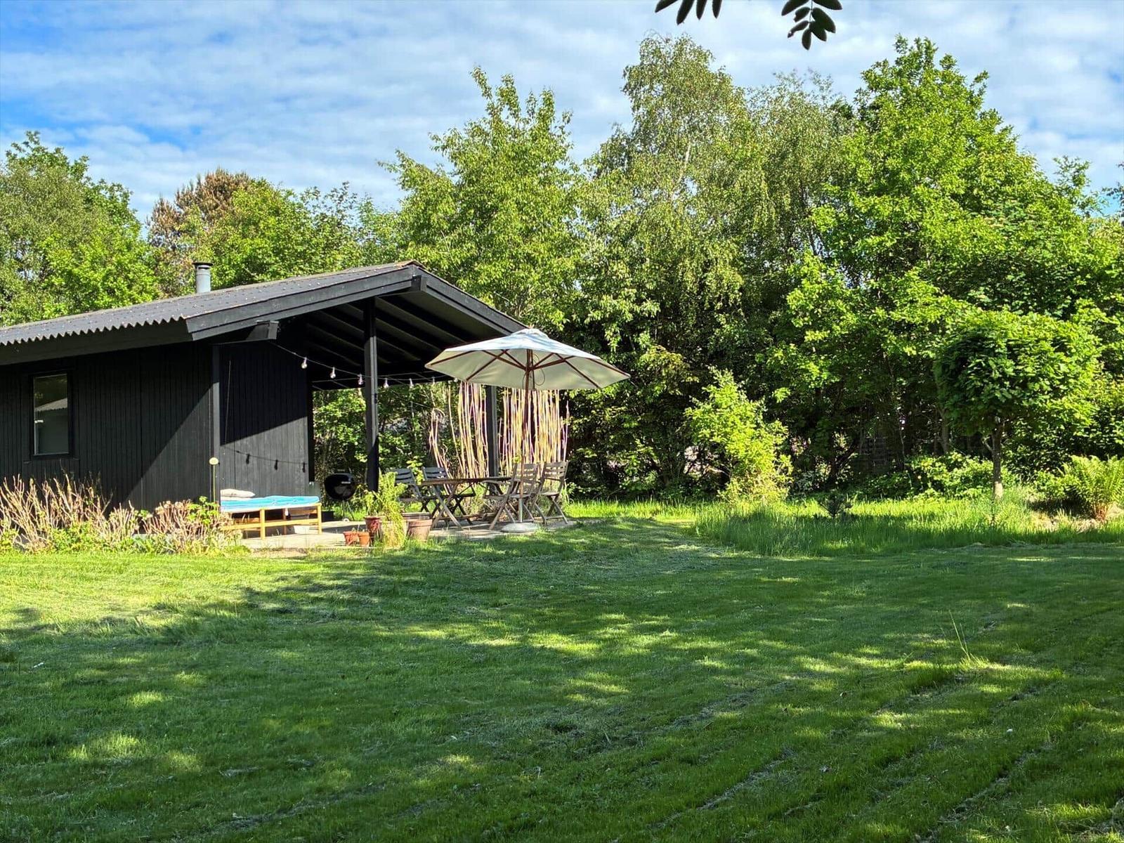 Black house with terrace, umbrella, and garden. Surrounded by trees and grass.