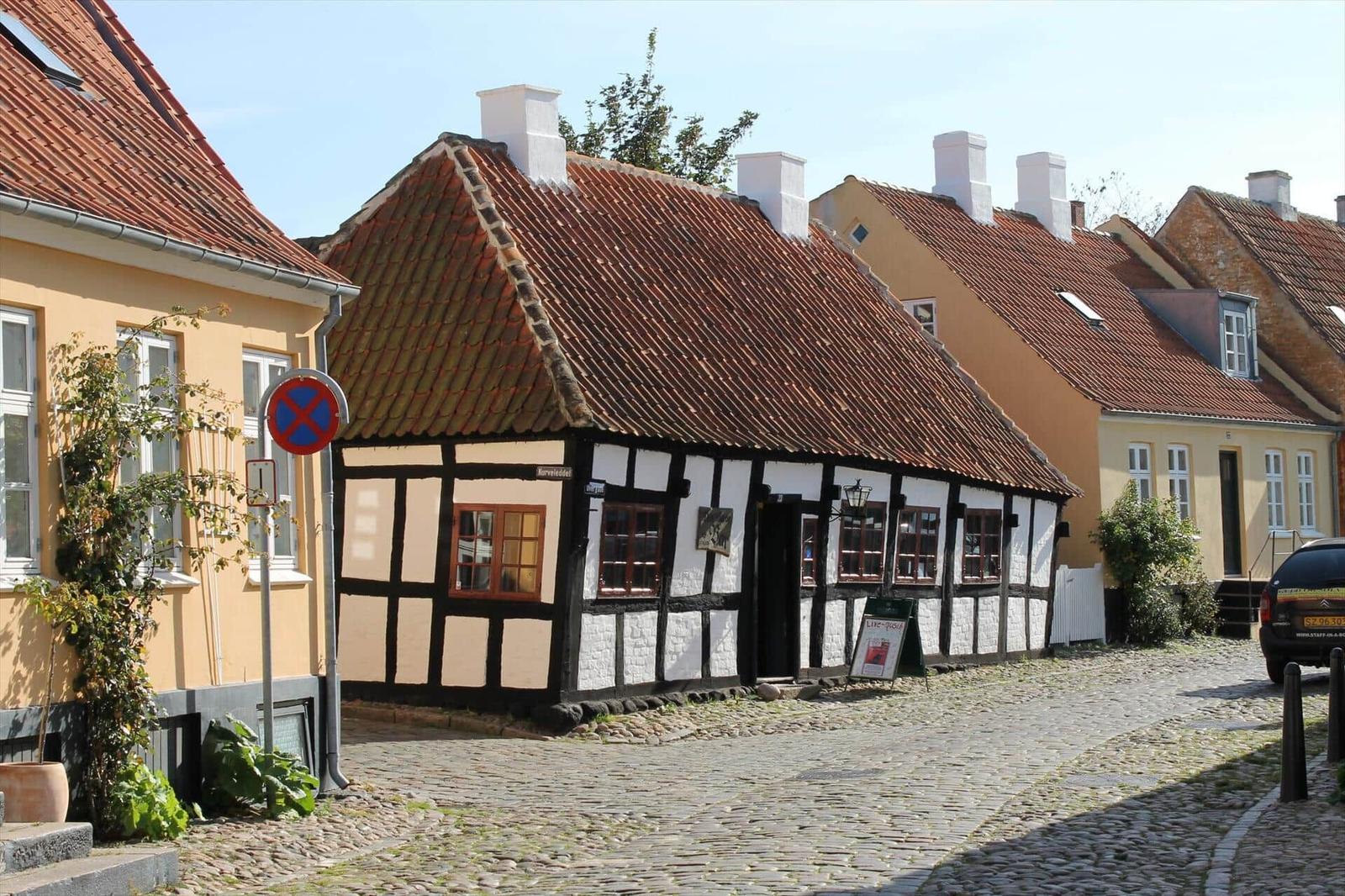 Traditional half-timbered house with red tiled roof and stone facade on a cobblestone street.