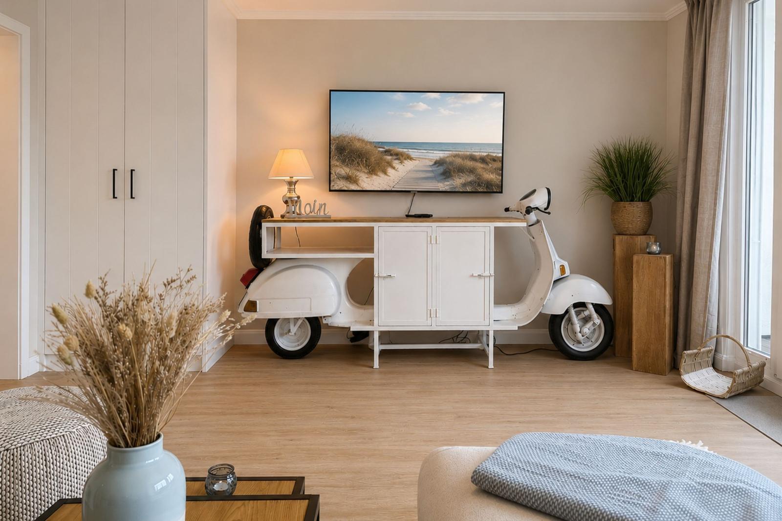 Wohnzimmer mit TV, weißen Schränken und einem weißen Roller.