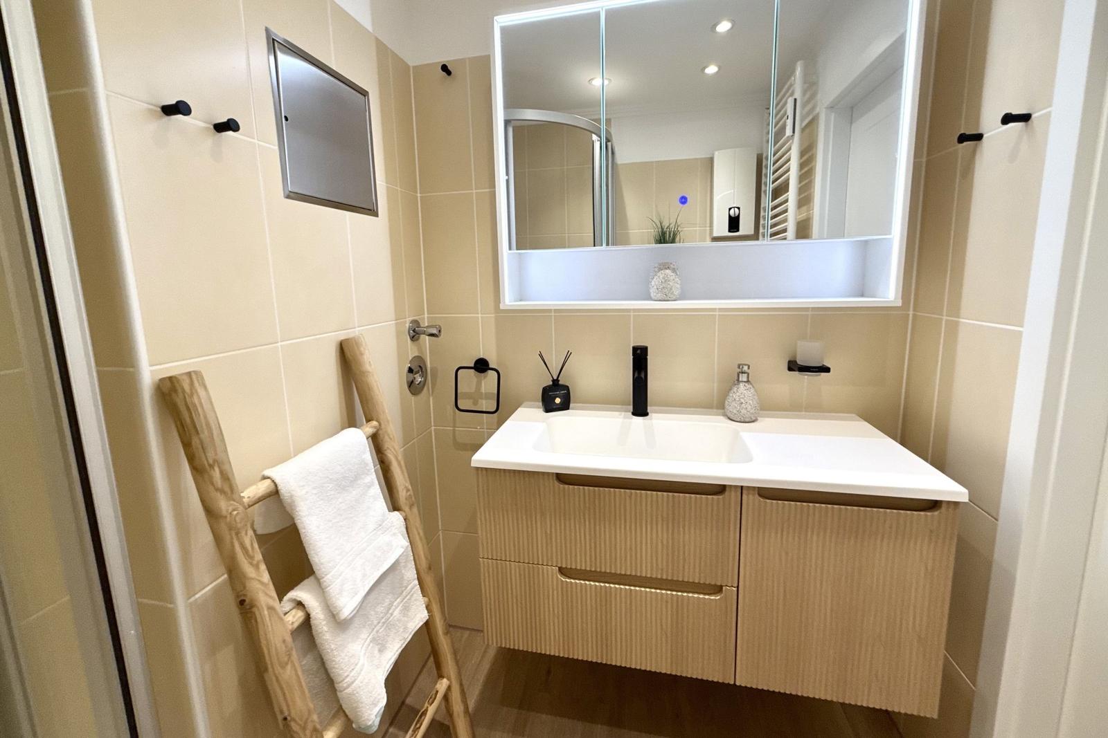 Badezimmer mit Waschtisch, Spiegel und Holzhandtuchständer.