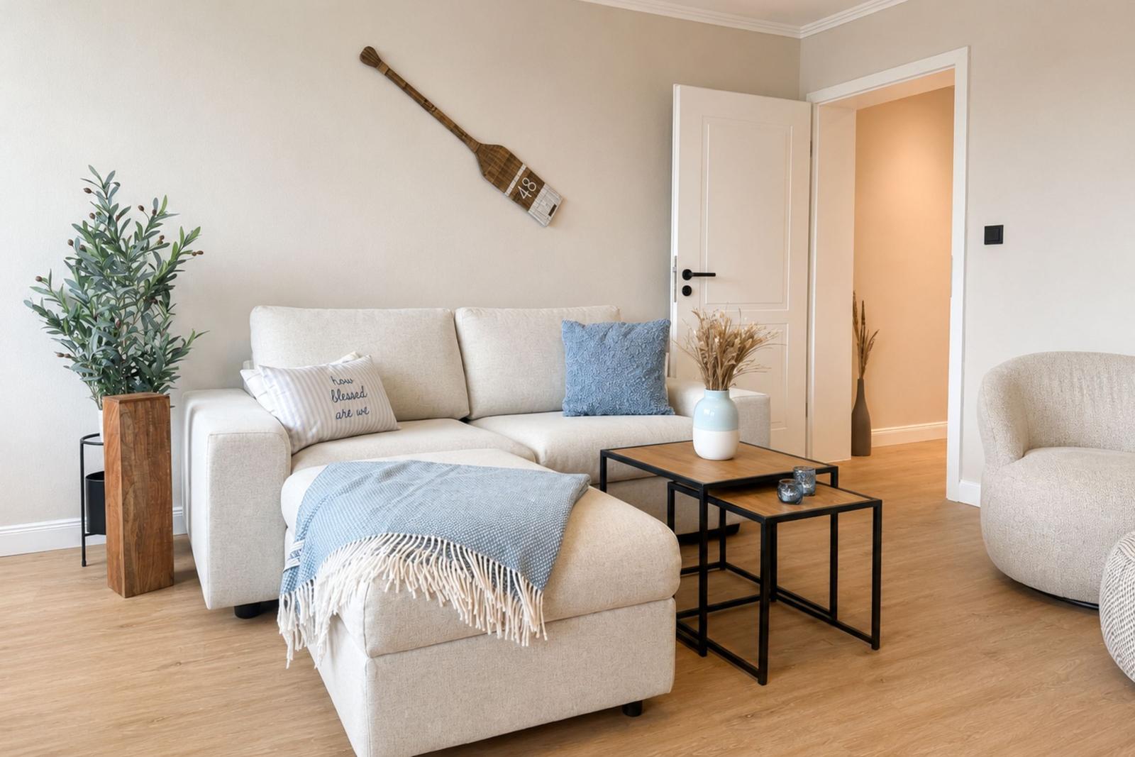 Wohnzimmer mit Sofa, Kissen und Tisch. Wanddekoration und Pflanzen sichtbar.