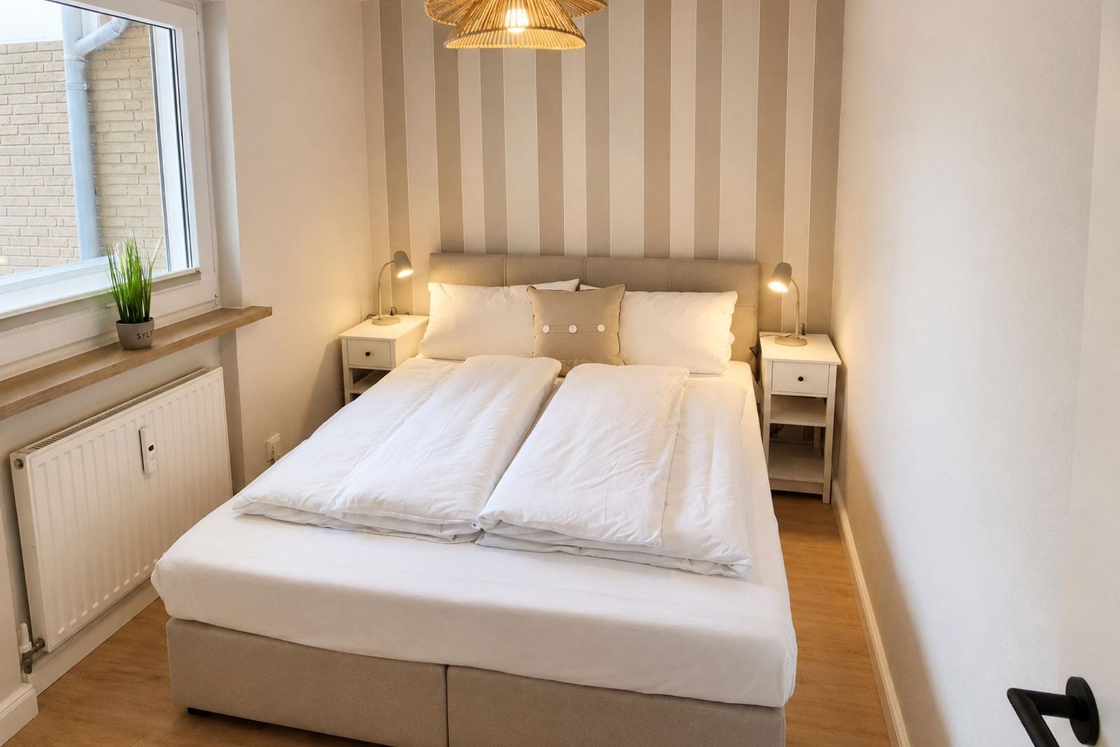 Schlafzimmer mit Doppelbett, zwei Nachttischen und Streifenwand