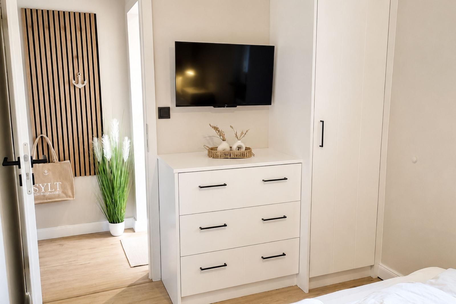 Schlafzimmer mit weißem Schrank, TV und Pflanze