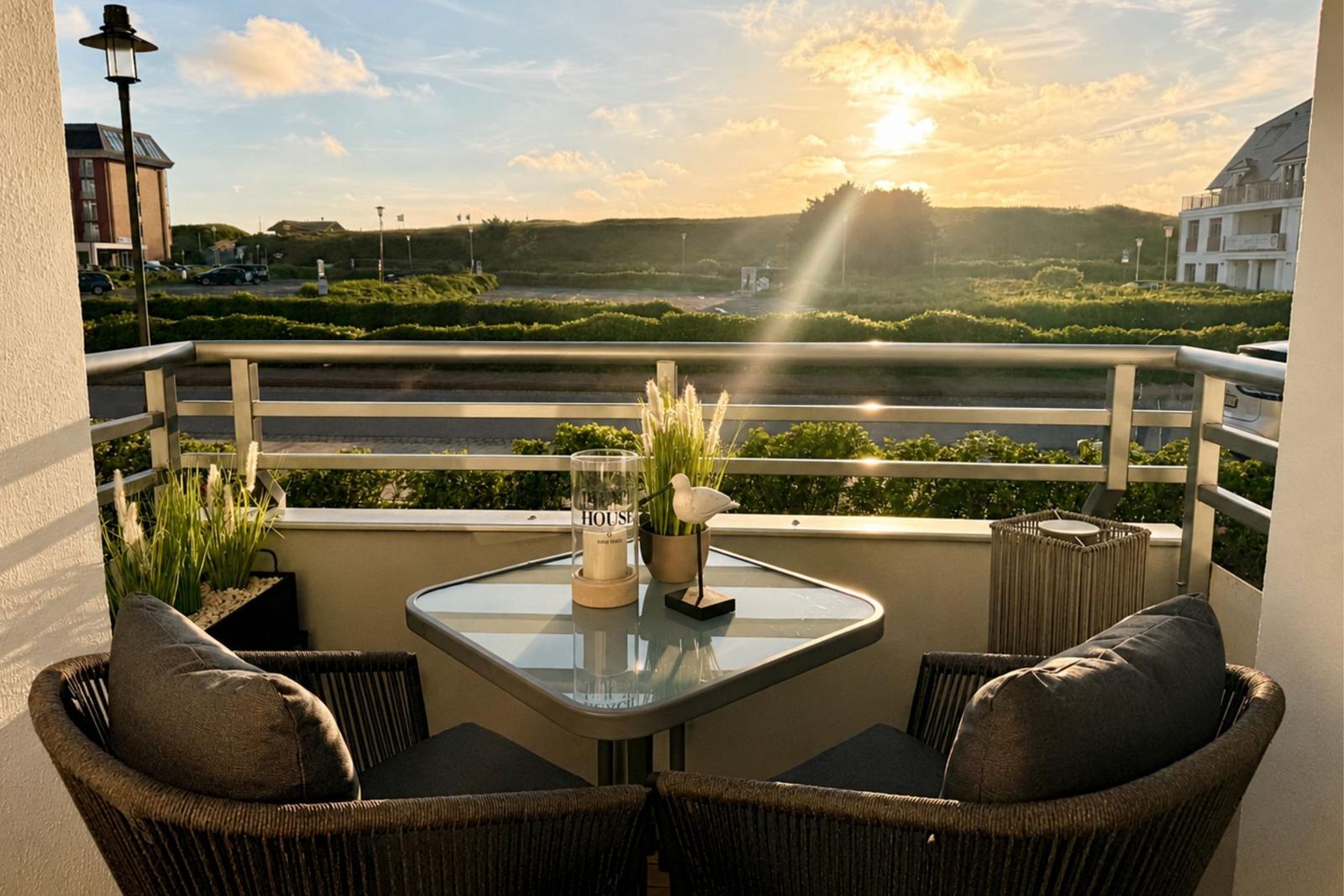Terrasse mit Tisch und zwei Stühlen, Blick auf Grünflächen und Sonnenuntergang.
