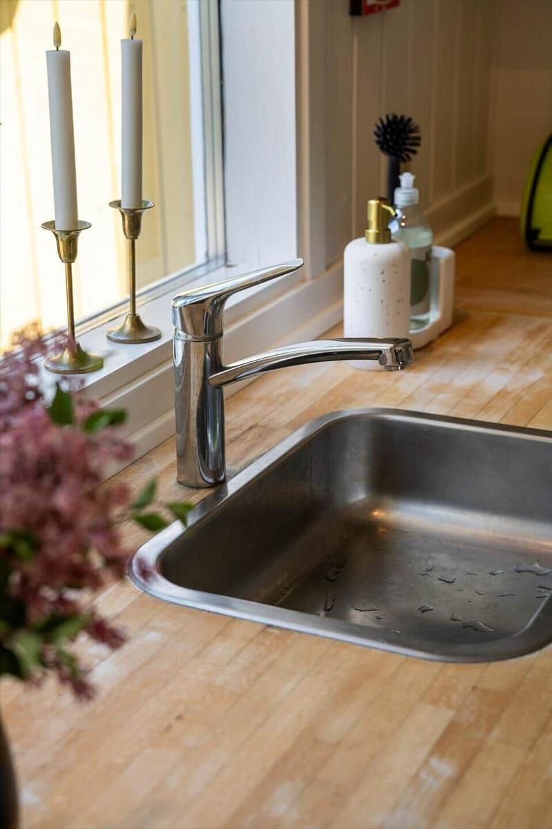 Edler Edelstahl-Spüle mit modernem Wasserhahn auf Holzoberfläche. Zwei Kerzenhalter und Blumen im Vordergrund.