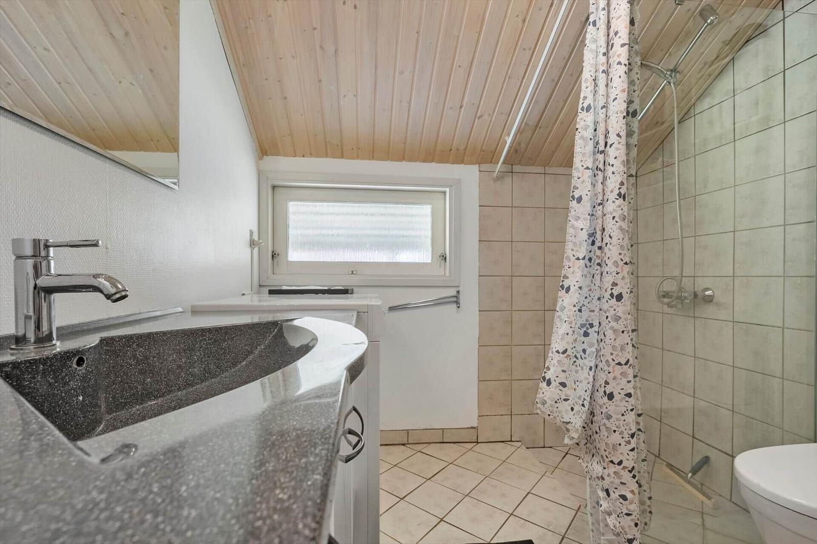 Badezimmer mit Dusche, Waschbecken und Toilette unter Holzdecke.