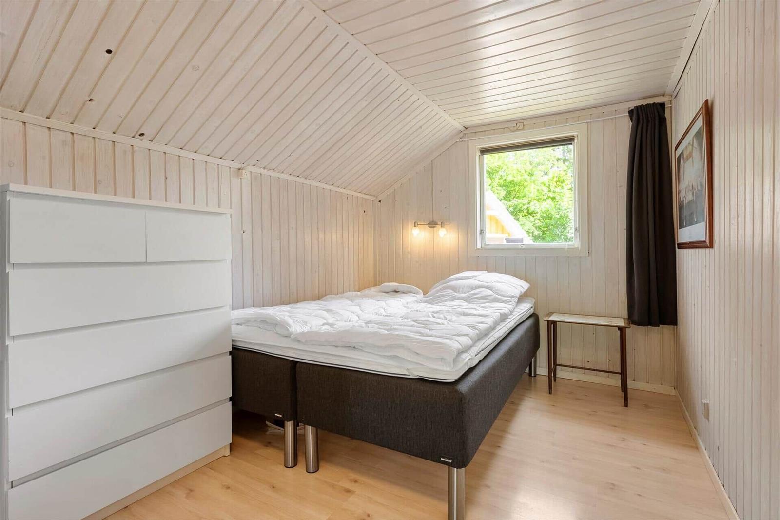 Schlafzimmer mit Bett, Schrank und Fenster. Holzwände und -decke.