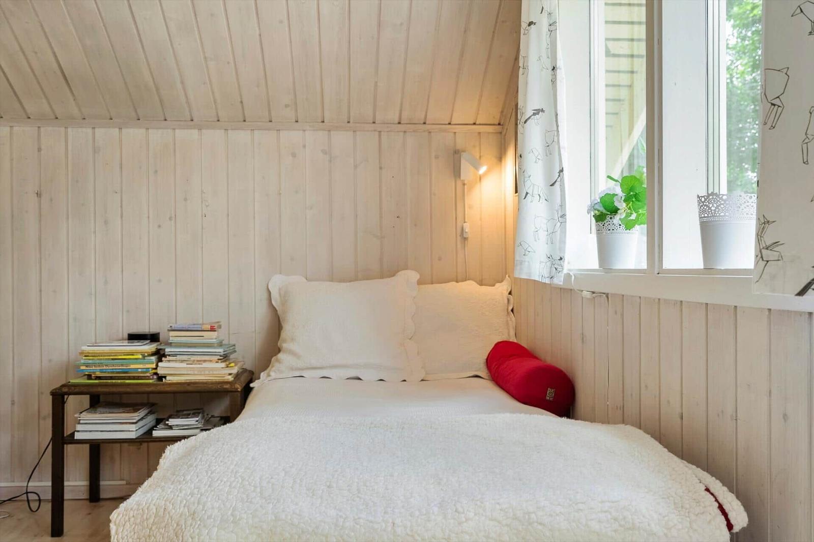 Schlafzimmer mit Bett, Bücherregal und Fenster mit Pflanze.