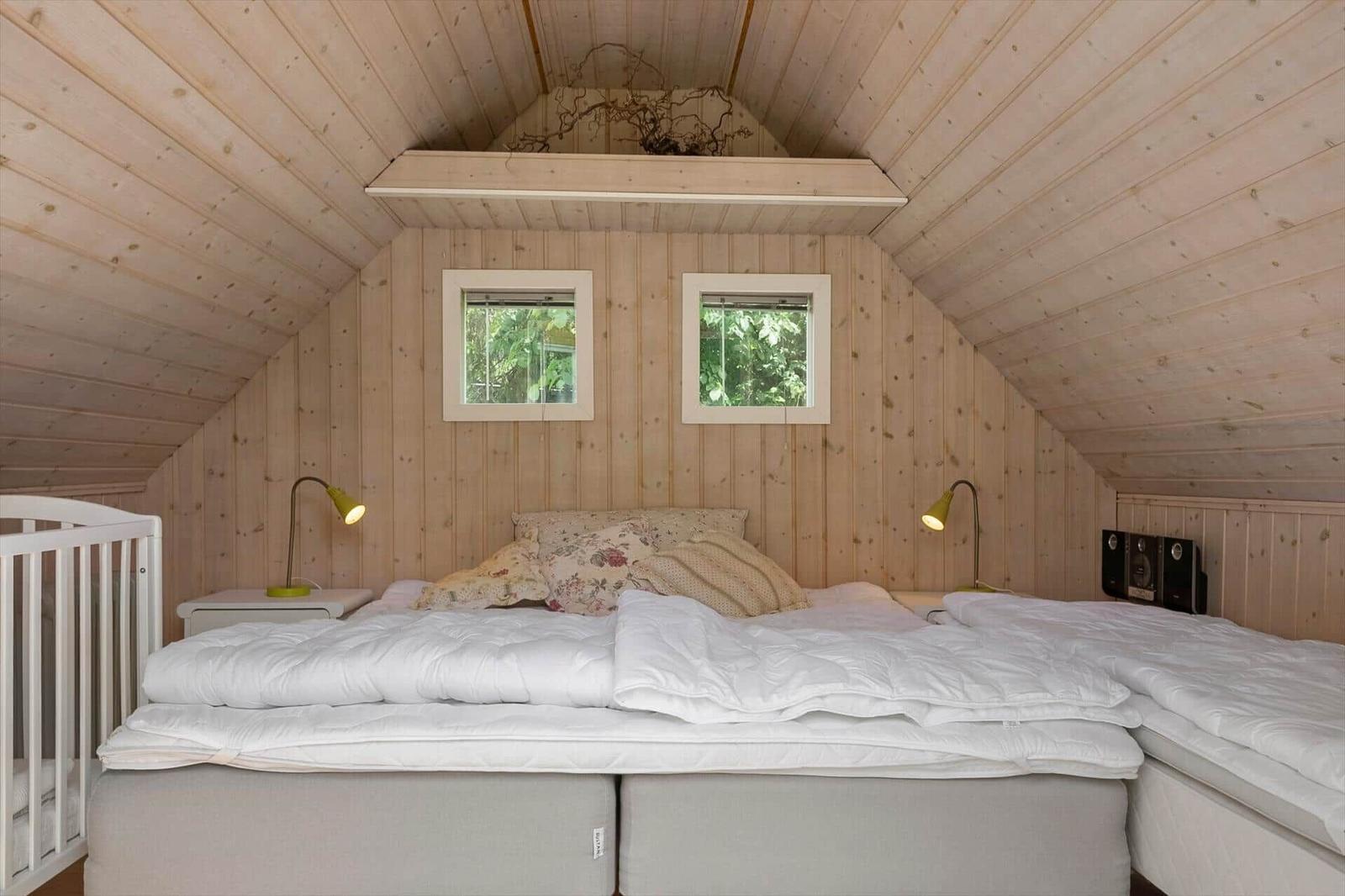 Schlafzimmer mit Holzwand, zwei Fenstern und Bett mit weißen Bettwäsche.