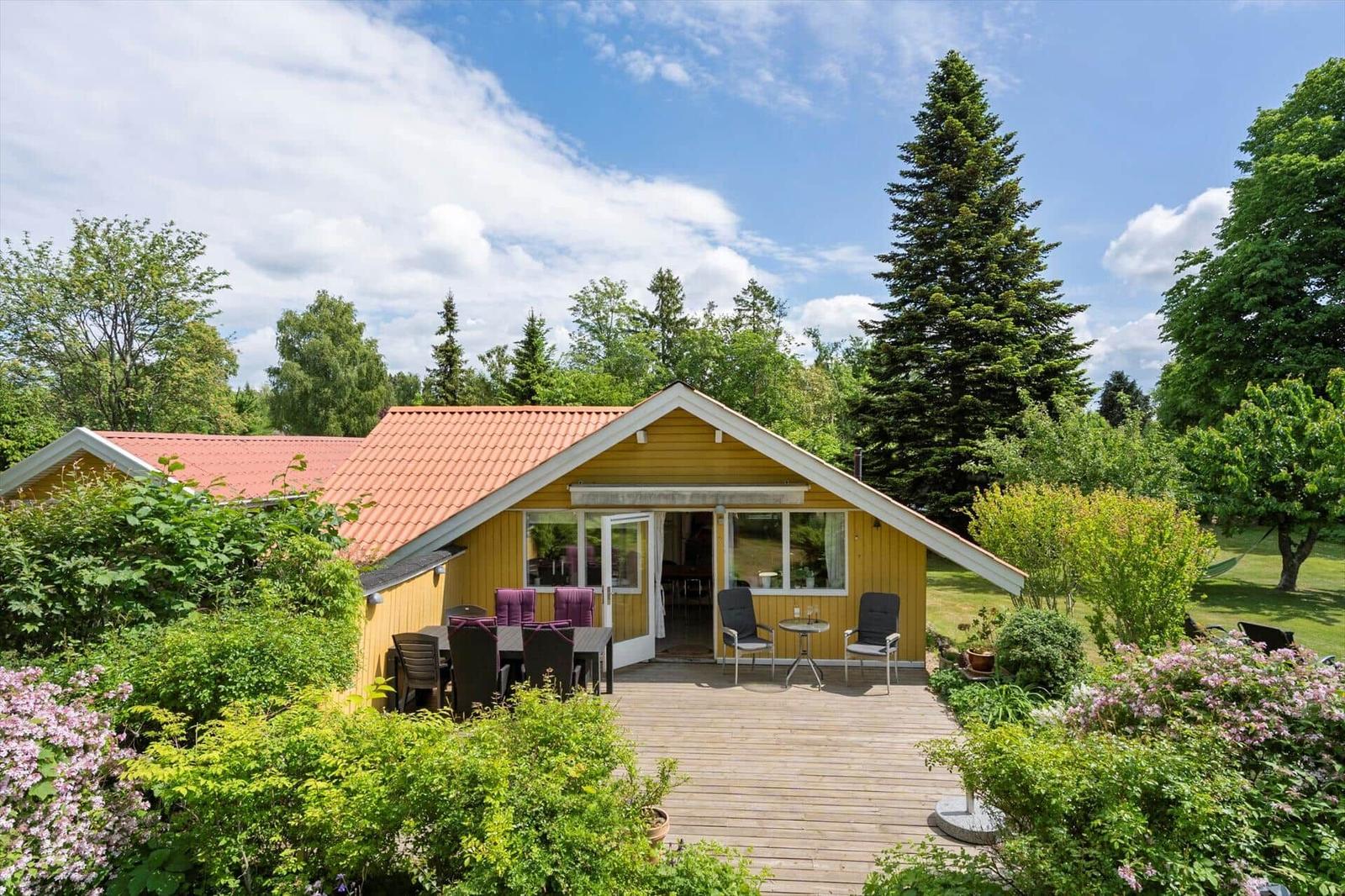Ein gelbes Haus mit Terrasse und Garten. Möbel stehen draußen. Bäume umgeben das Grundstück.