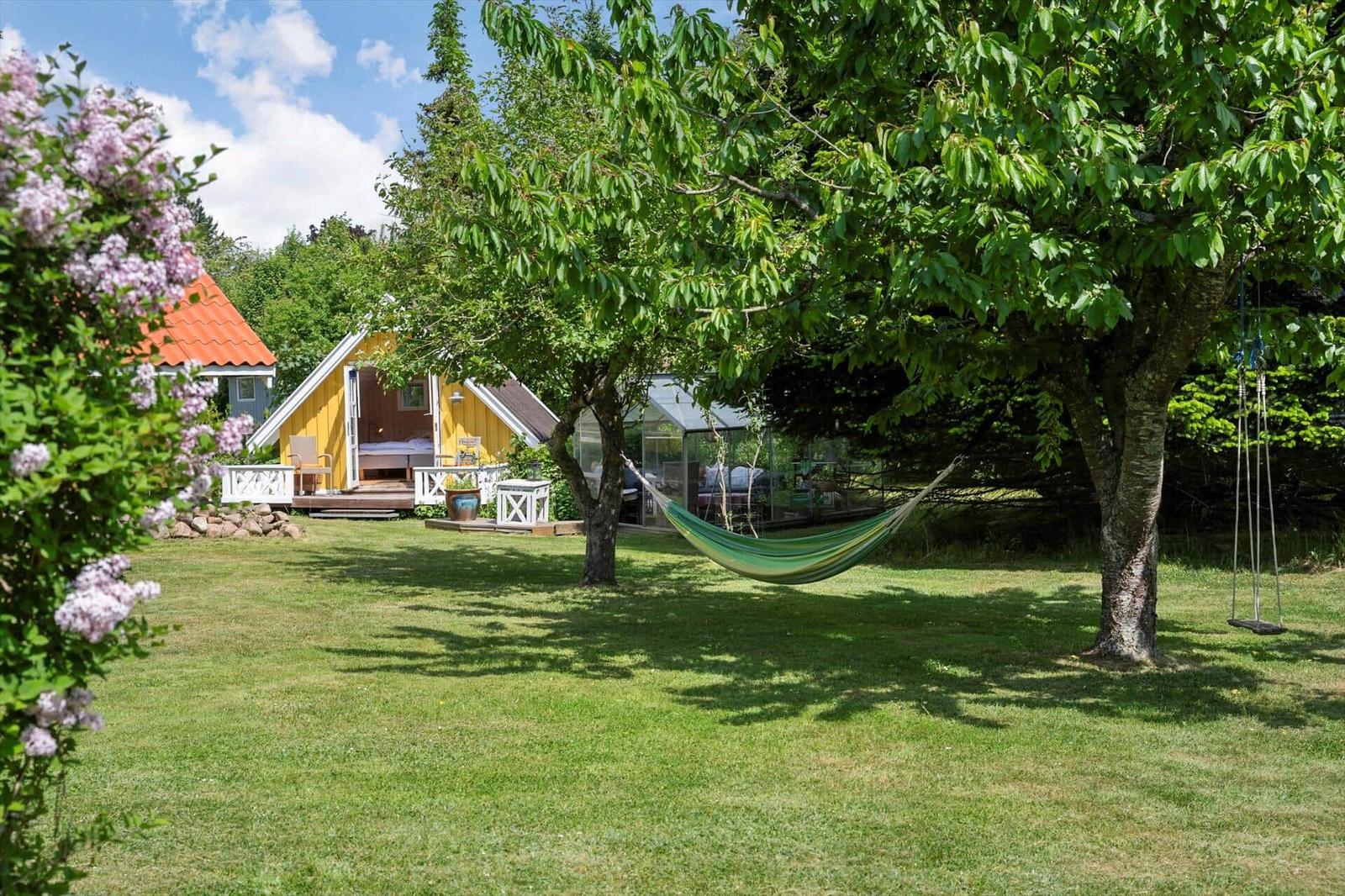 Hängemattenschau in grünem Garten mit gelbem Haus und Baum