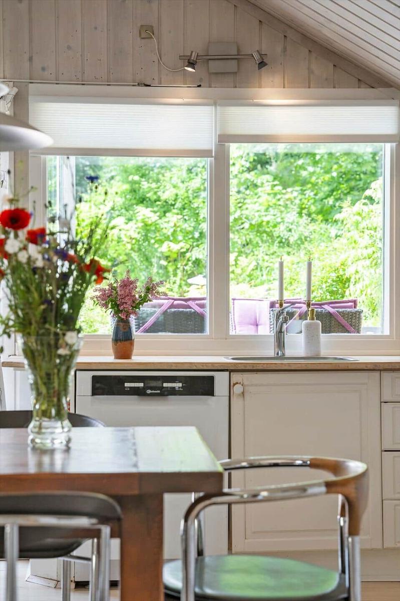 Küche mit Holzwand, Fenster und Tisch. Blumen und Spüle sind sichtbar.