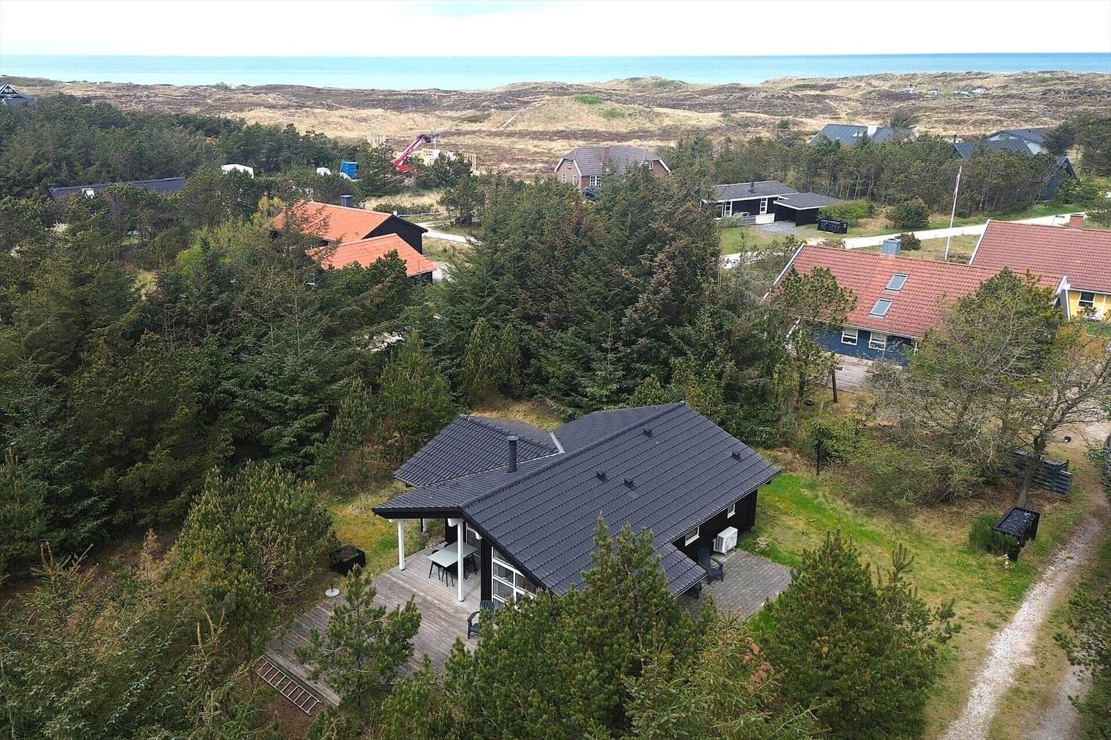 Haus mit Terrasse umgeben von Bäumen, Blick auf Strand und Dünen.