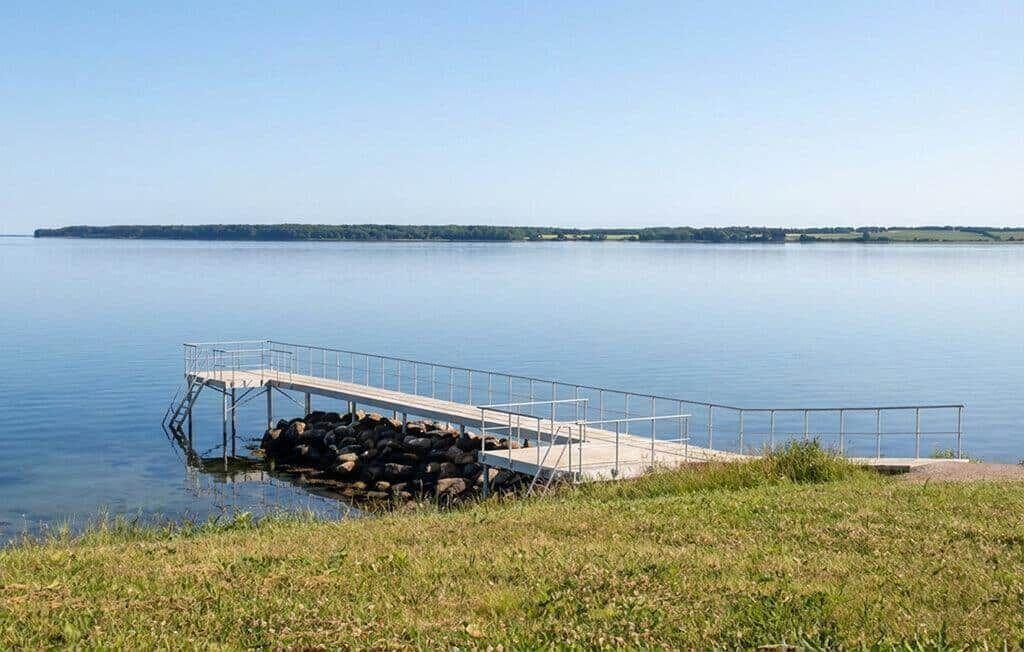 Ein hölzerner Steg führt ins Wasser. Im Hintergrund erstreckt sich eine grüne Insel.
