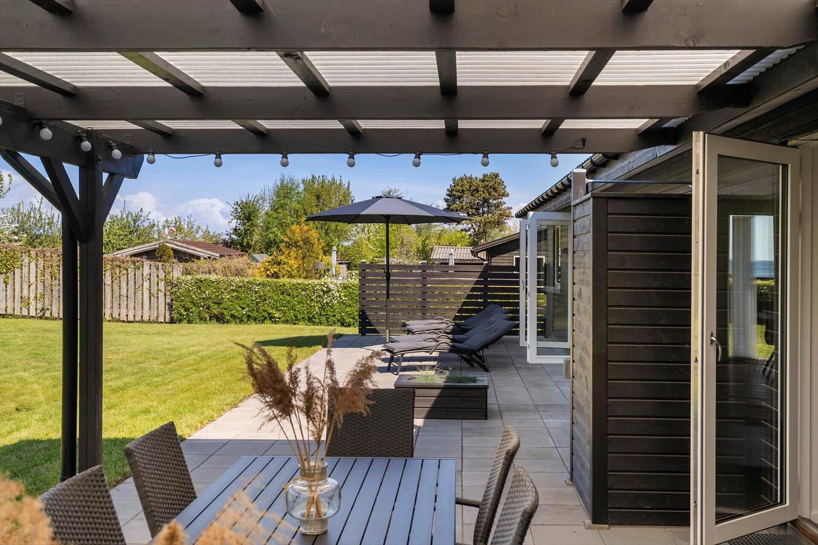 Terrasse mit Pavillon, Tisch, Stühlen, Sonnenschirm und Liegen. Blick auf grünen Garten.