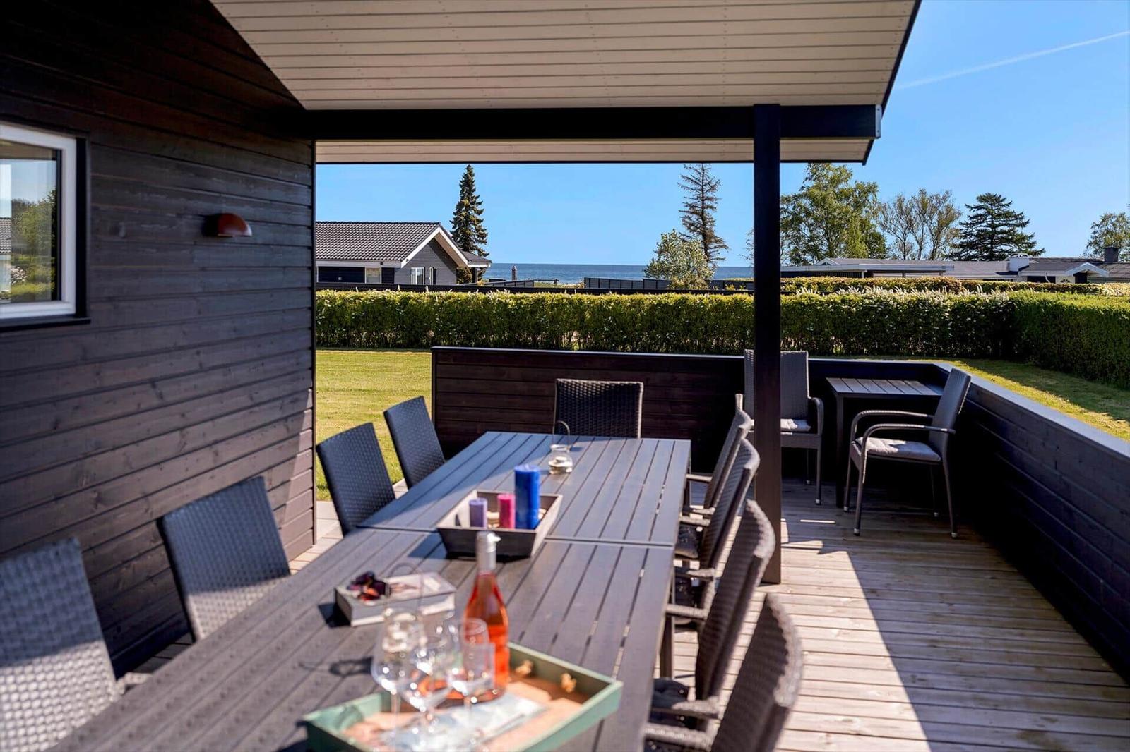 Terrasse mit Tisch und Stühlen, Blick auf Grünflächen und Meer.