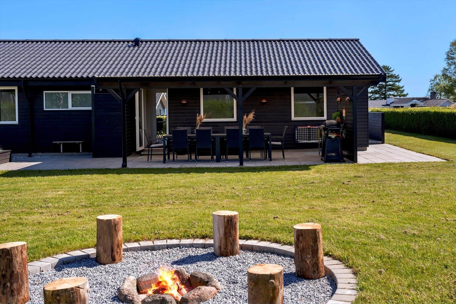 Haus mit Terrasse, Grill und Feuerstelle im Garten.