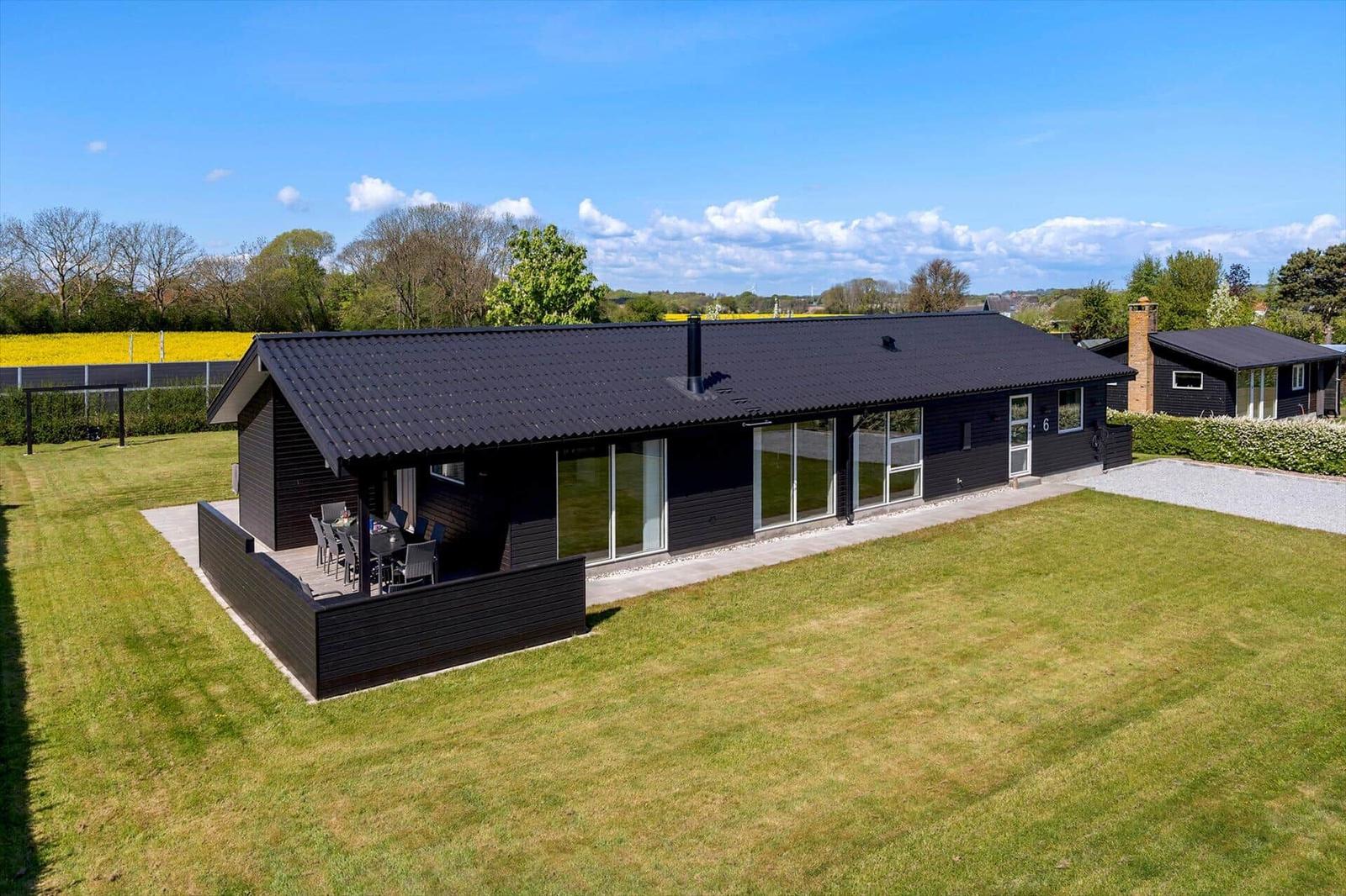 Moderne Villa mit Terrasse und Garten. Große Fenster und schwarze Fassade.