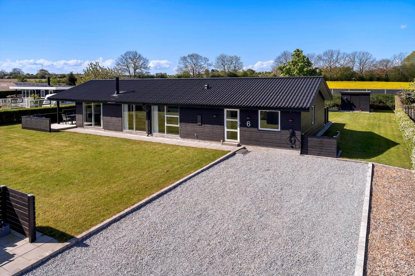 Moderne Villa mit großem Garten und Terrasse. Schwarze Fassade und Dach. Grasfläche und Kiesweg.