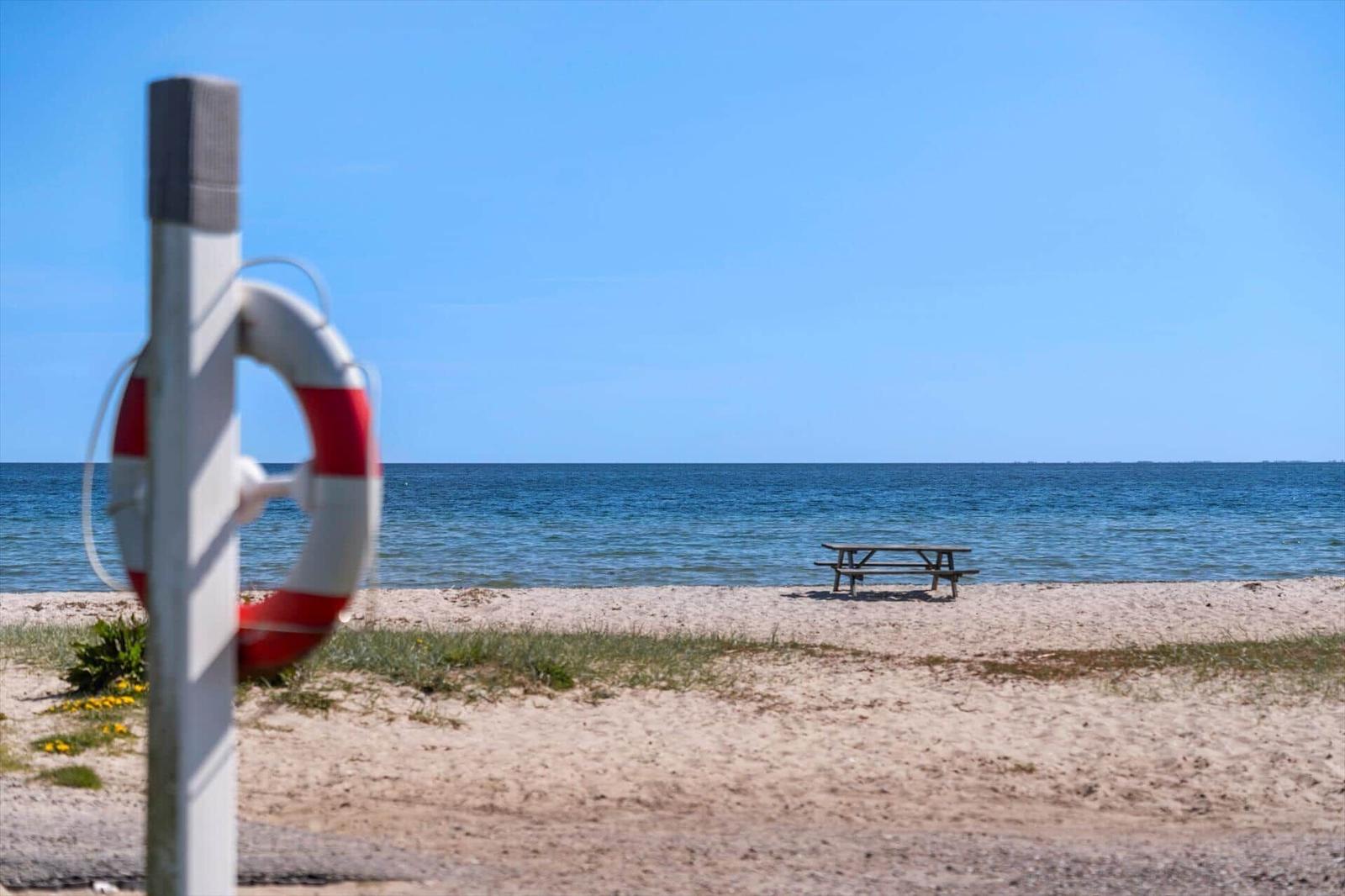 Strand mit Rettungsring, Picknicktisch und Meer unter blauem Himmel.