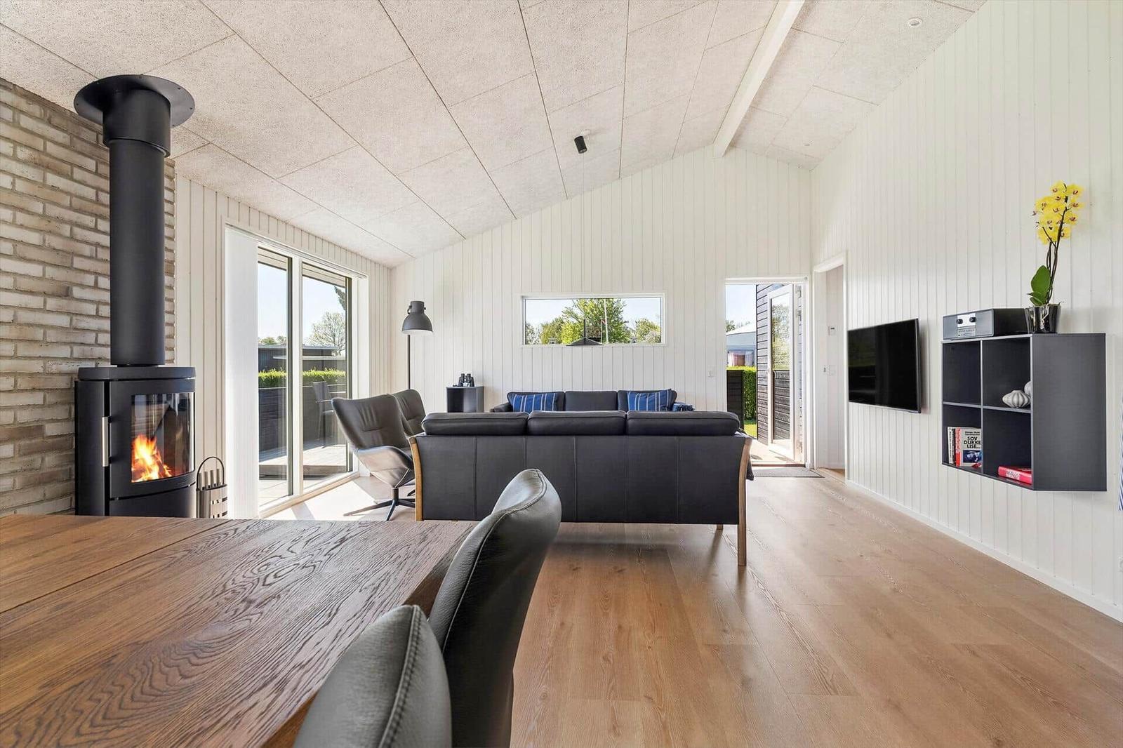 Wohnzimmer mit Sofa, Kamin und Holzboden. Fenster und Tür zur Außenterrasse.