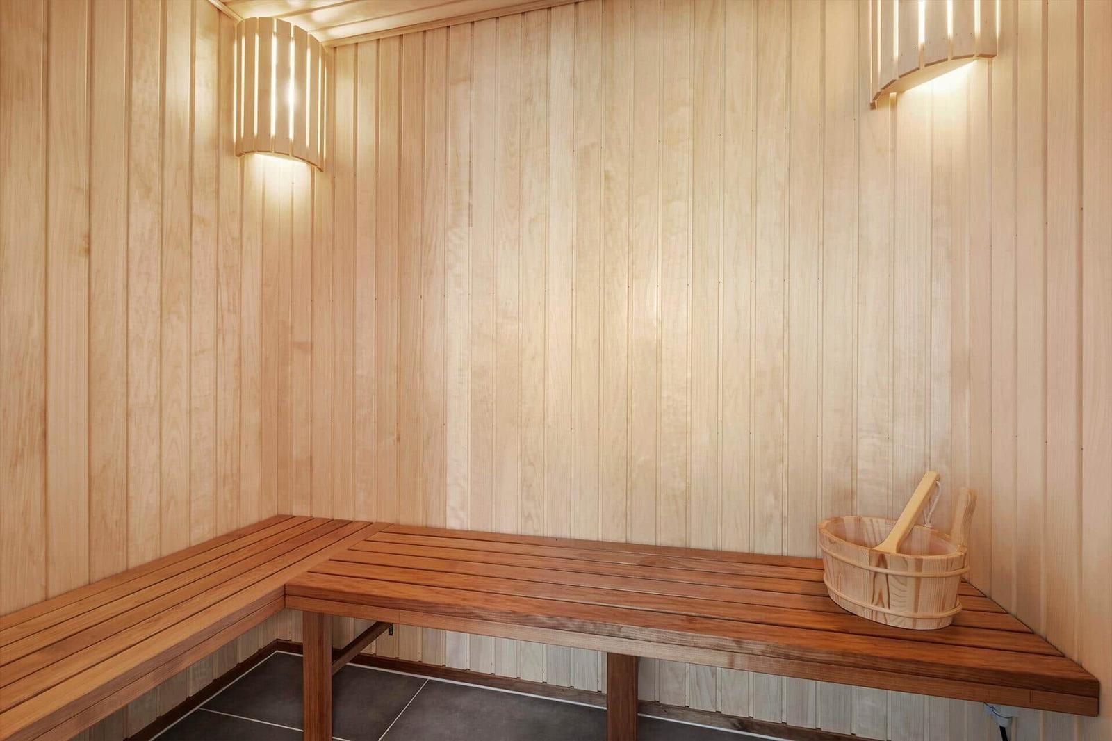 Sauna mit Holzwand, Sitzbank und Eimer mit Besen
