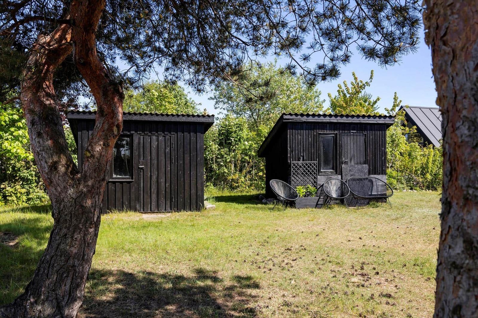 Two black wooden cabins with garden and seating under trees.