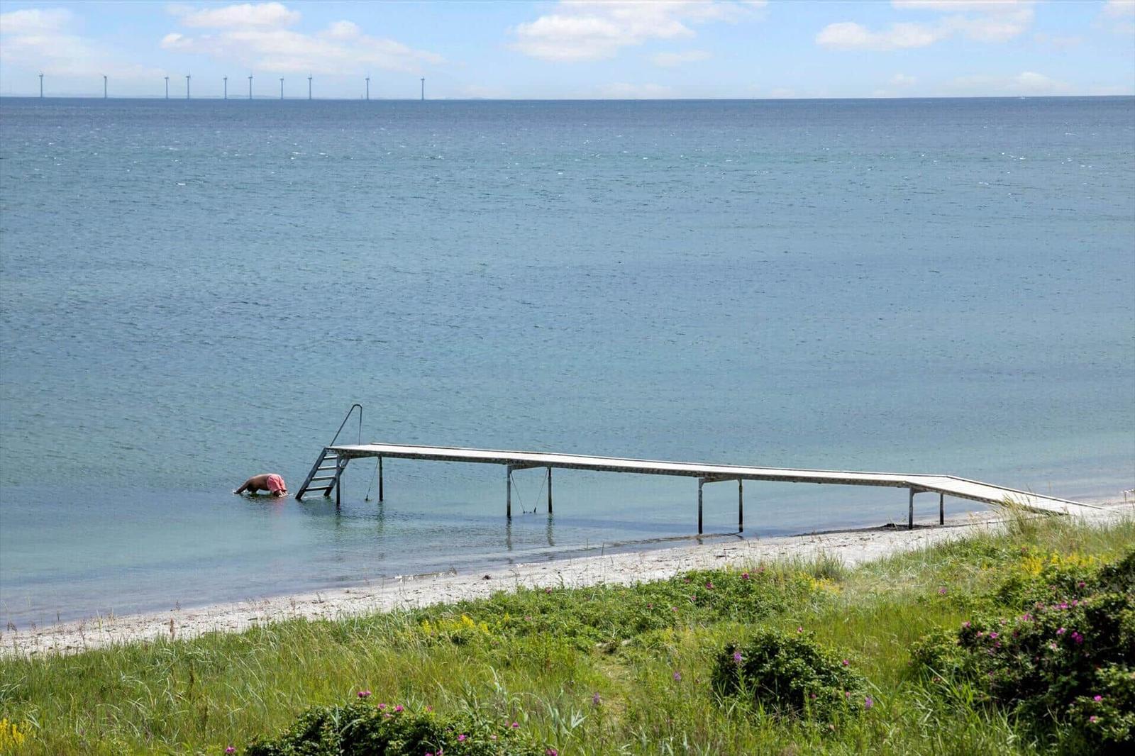 Ein Steg führt ins Wasser. Im Hintergrund sind Windkraftanlagen sichtbar.