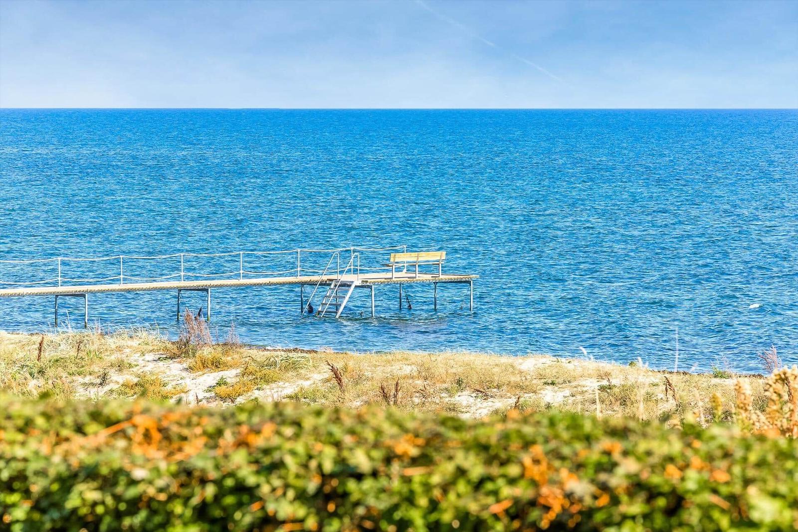 Ein hölzerner Steg mit Geländer und Sitzbank führt ins Meer.