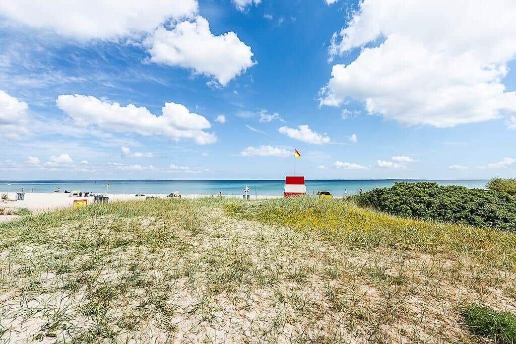 Strand mit Sanddünen, blauem Himmel und rotem Leuchtturm. Strandbad mit Sonnenschirmen.