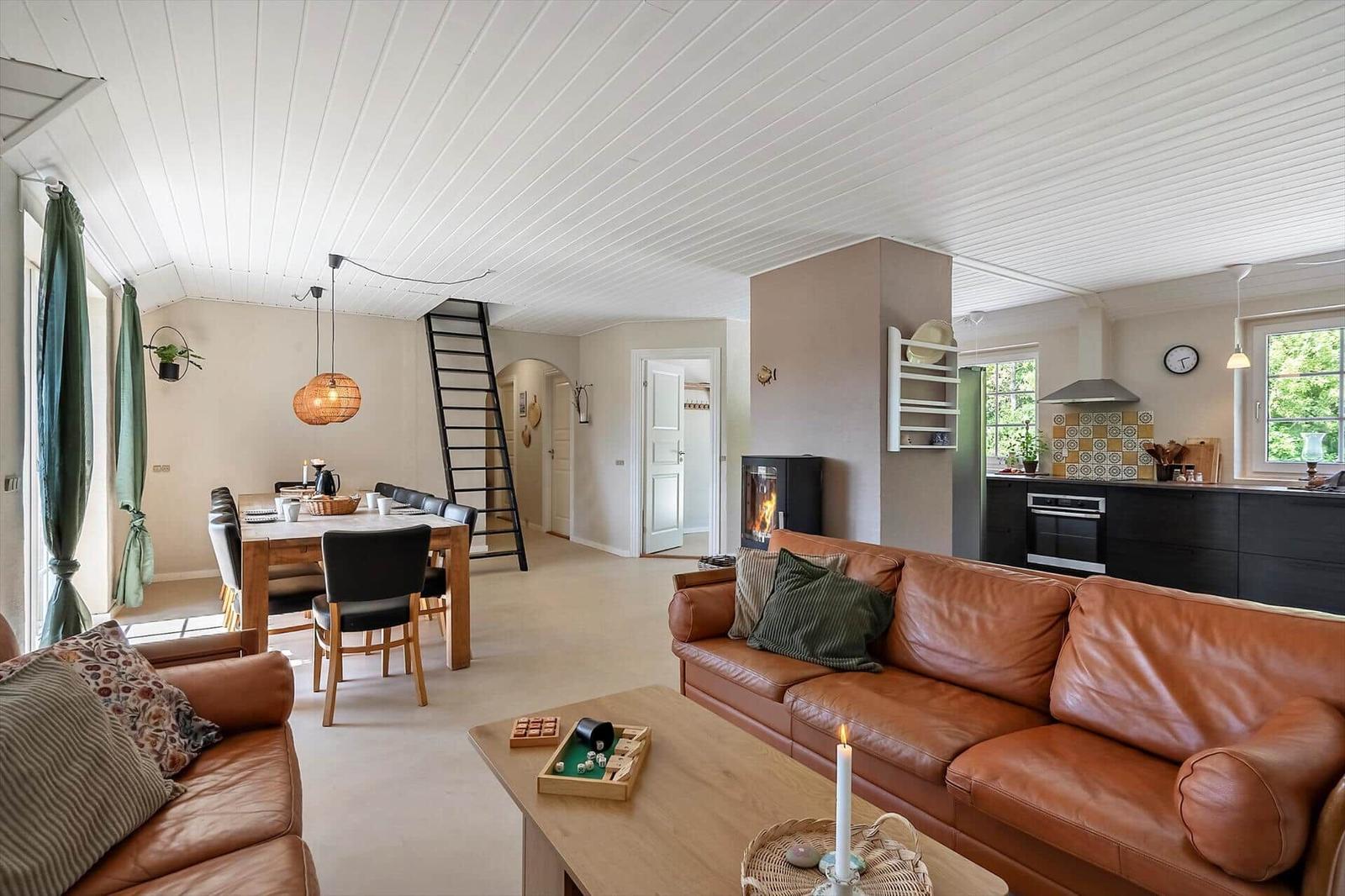 Wohn- und Essbereich mit Sofa, Tisch und Kamin. Küche mit Schränken und Fenster.