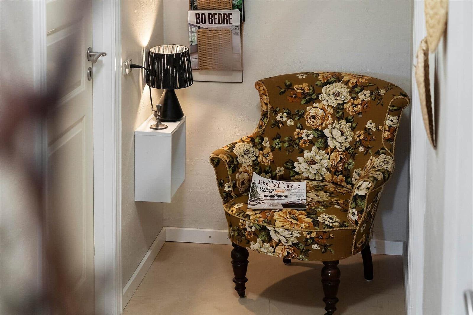 Florales Sessel mit Zeitschrift, schwarze Lampe und Wandhalterung im Flur.