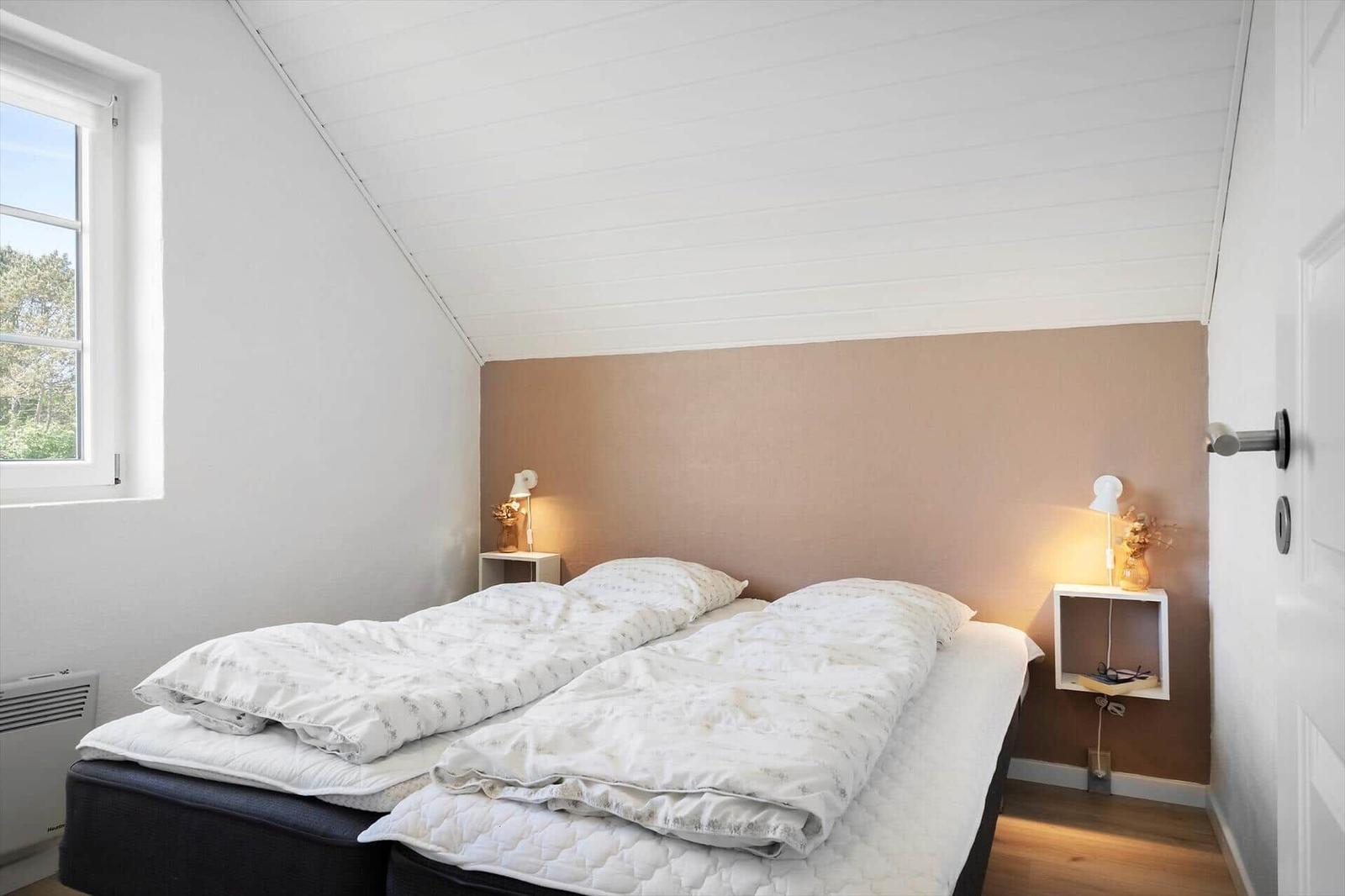 Schlafzimmer mit Doppelbett, Fenster und zwei Nachttischen mit Lampen.