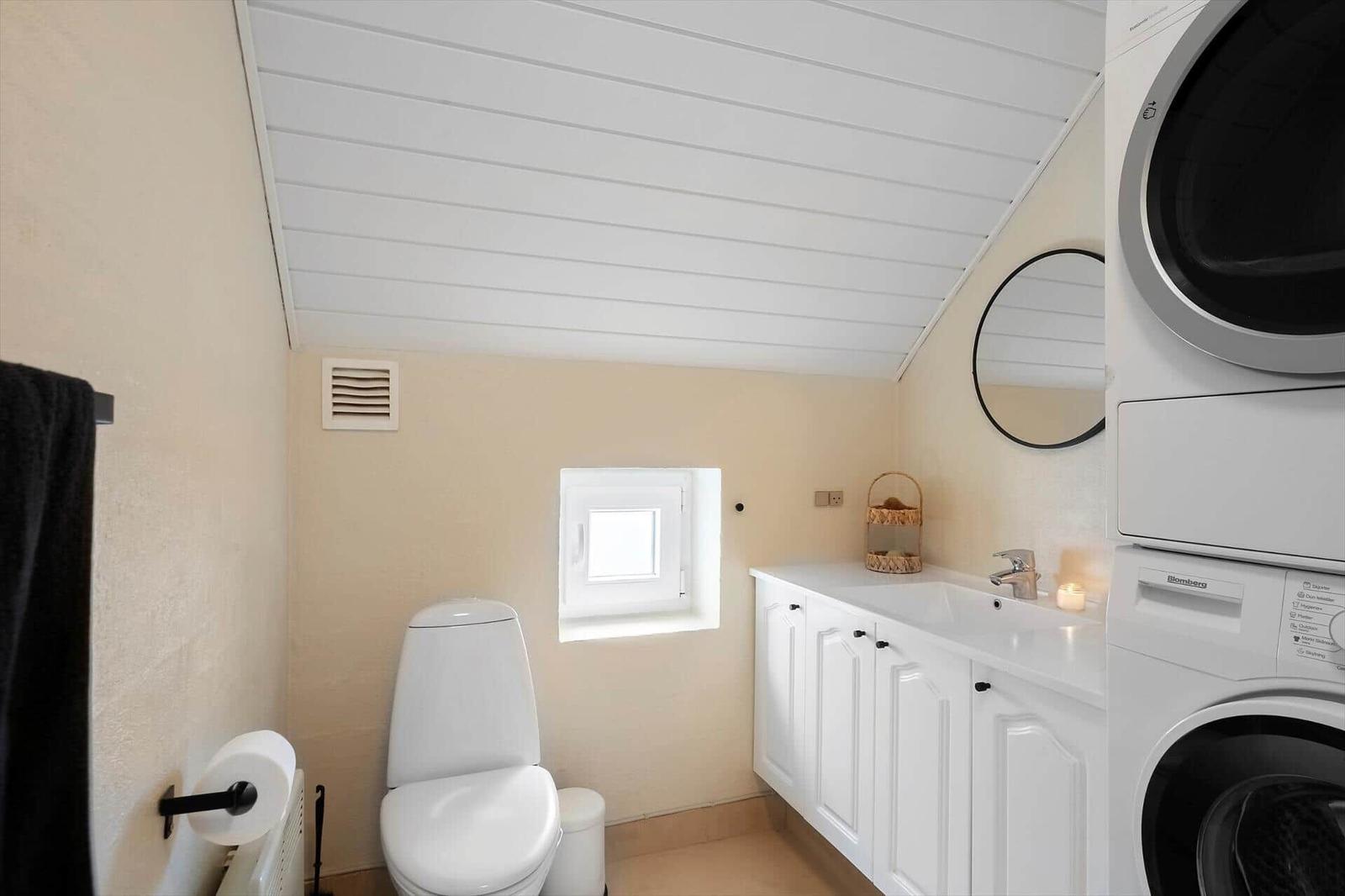 Badezimmer mit Toilette, Waschbecken und Wäschetrockner. Dachboden-Decke und kleines Fenster.